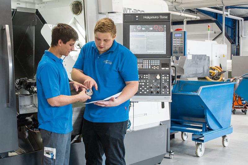 Zwei Mitarbeiter unterhalten sich über ein Präzisionsteil vor einer Maschine